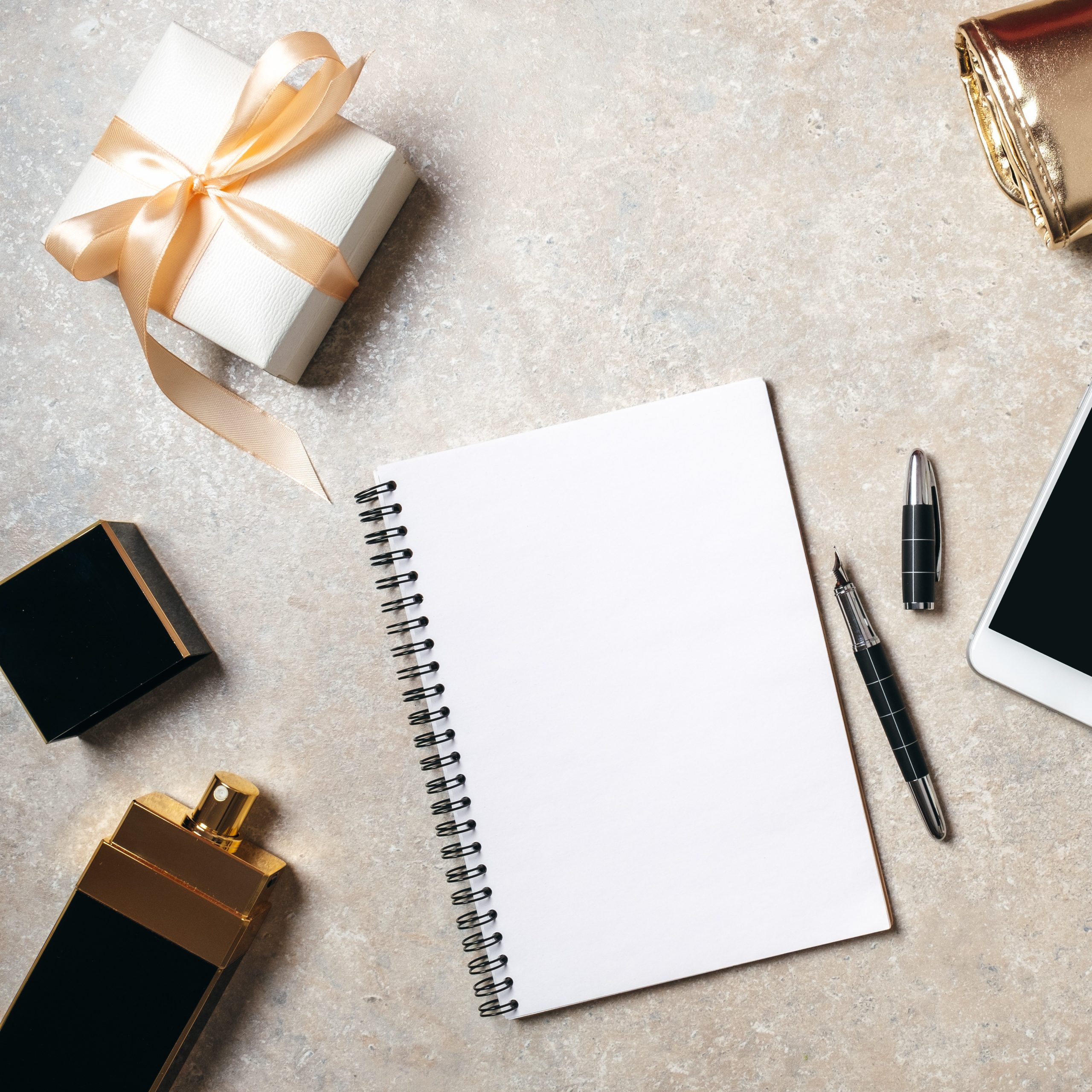 Flat lay notepad with copy space blank mockup. Top view home office desk workspace decorated with smartphone, golden feminine accessories, perfume bottle, gift box and stationery