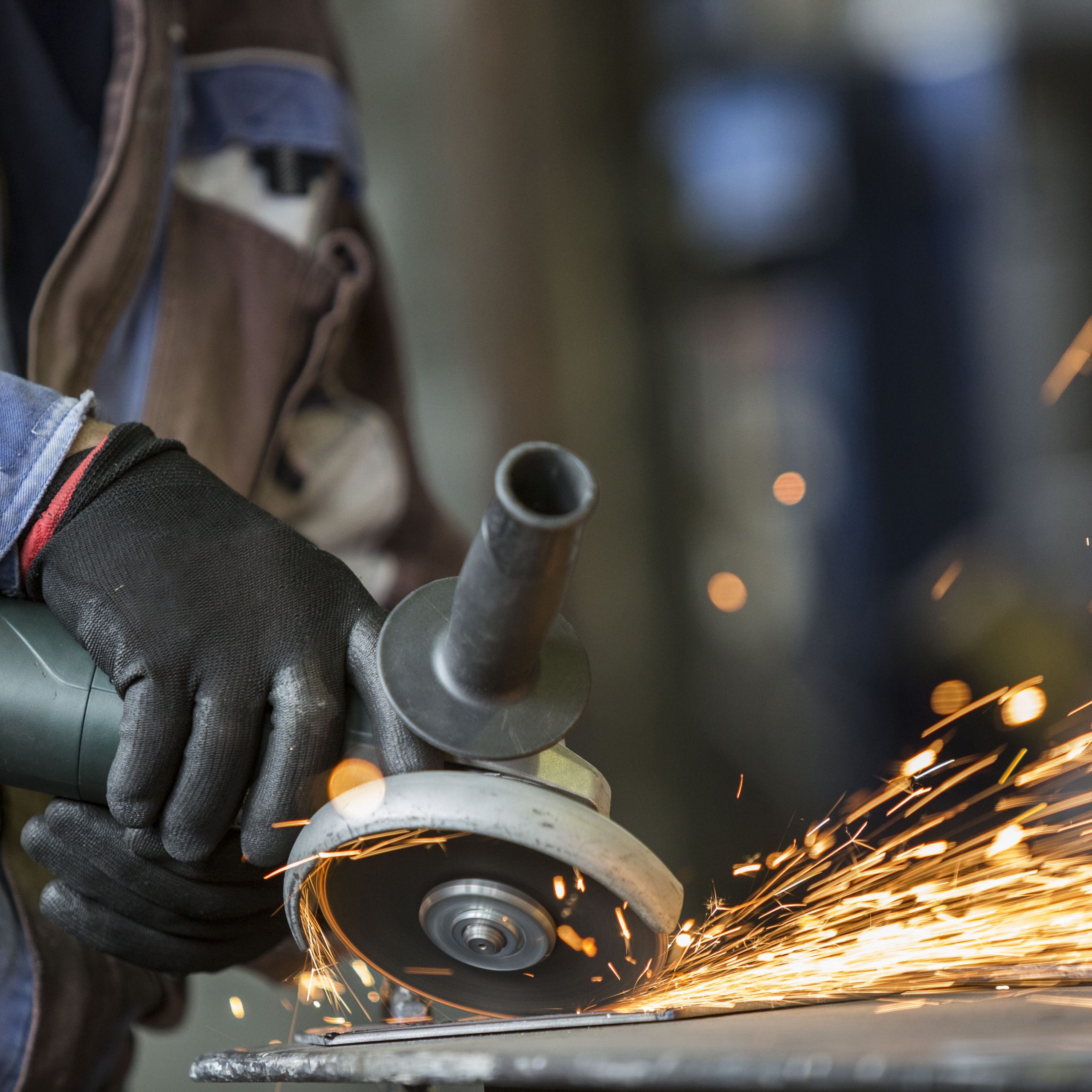 Closeup of the workman with a mask and gloves who is grinding a metal object with a grinder. He wears a protective wardrobe.