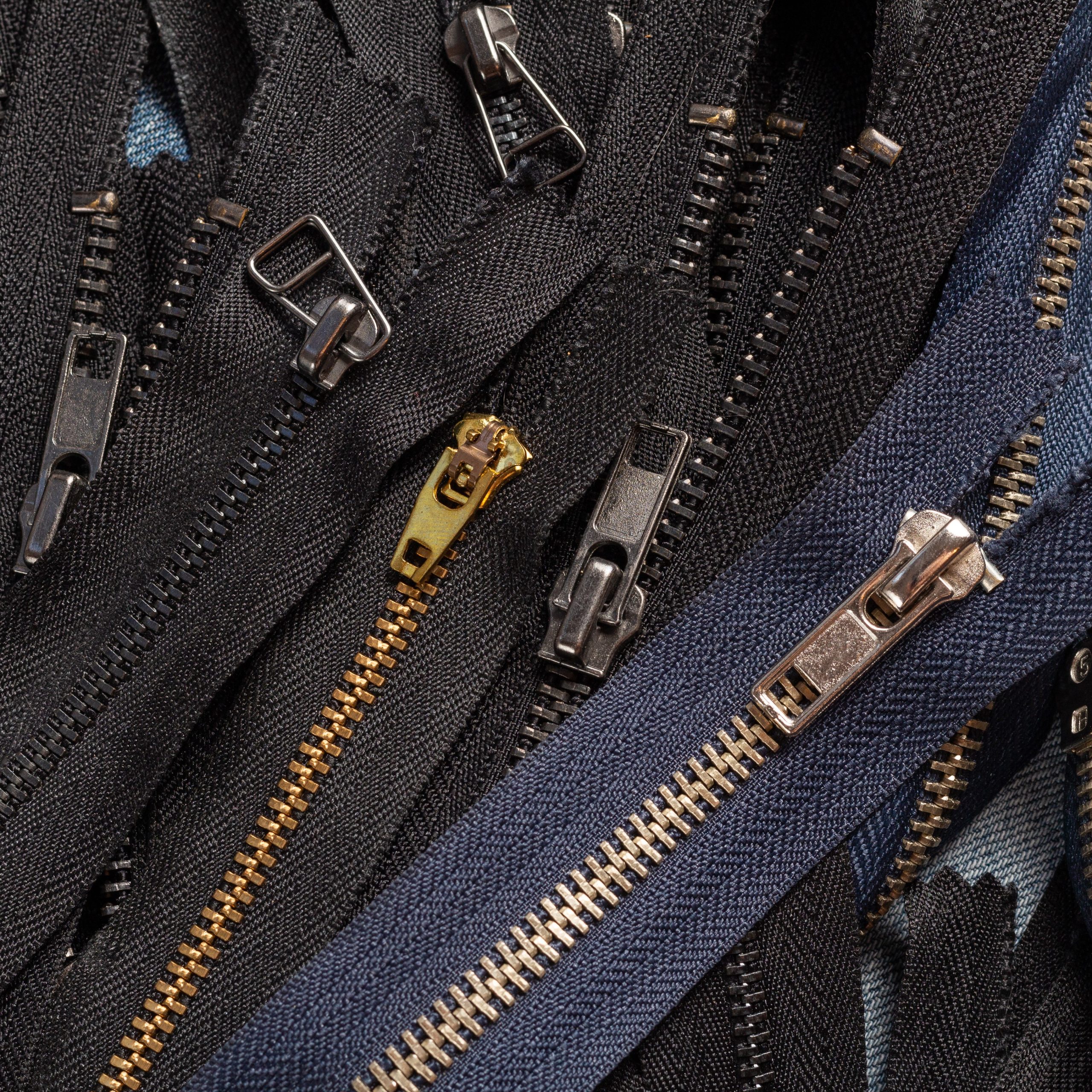 Pack a lot of black navy metal brass antique zippers stripes with sliders pattern for handmade sewing tailoring leathercraft on the blue wooden background