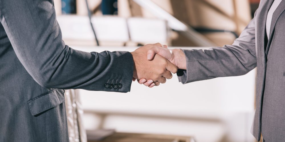 cropped view of businesspeople shaking hands in warehouse